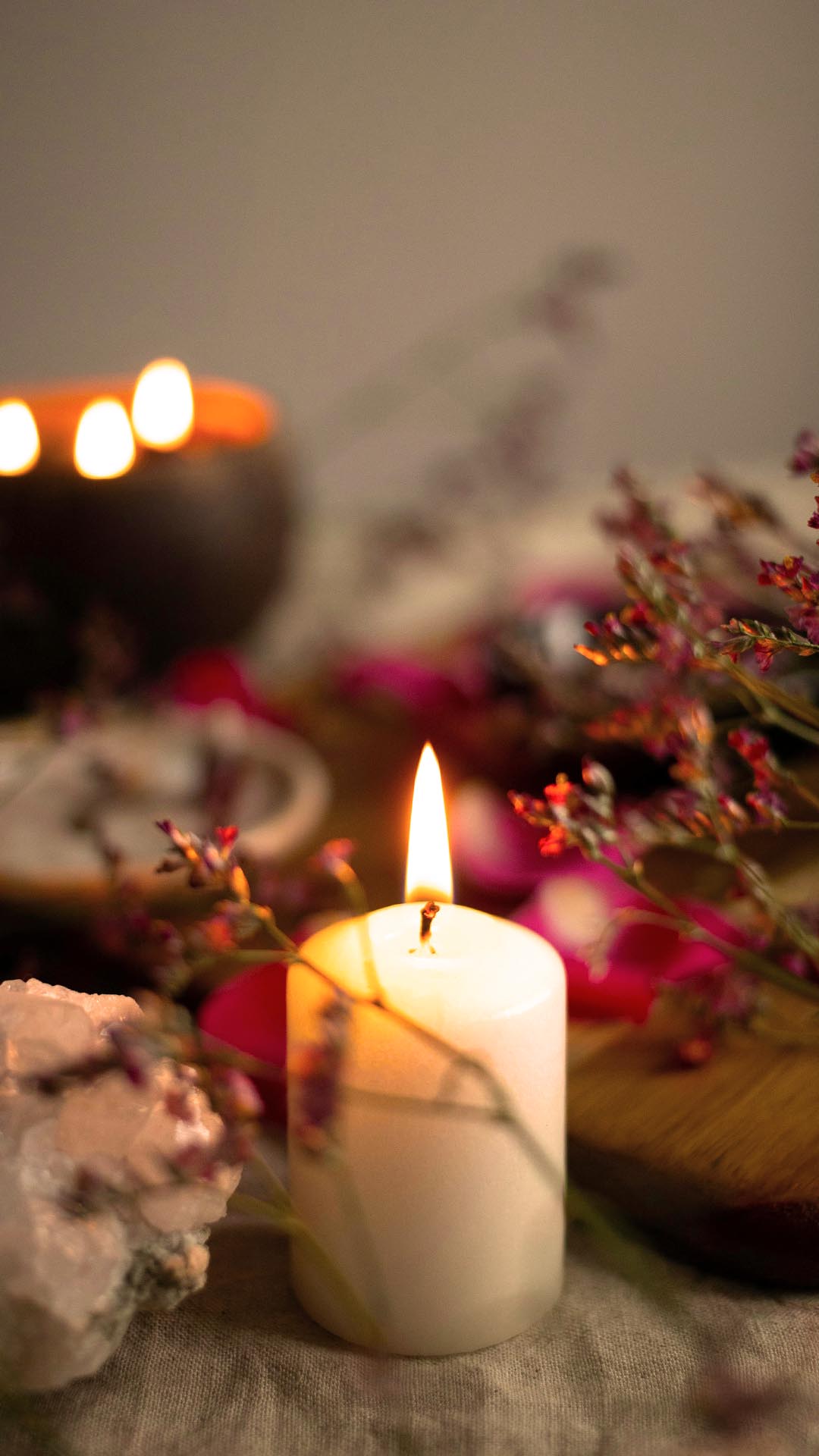 Lit white candle surrounded by flowers and crystals, creating a peaceful sacred space for tantric rituals at home.